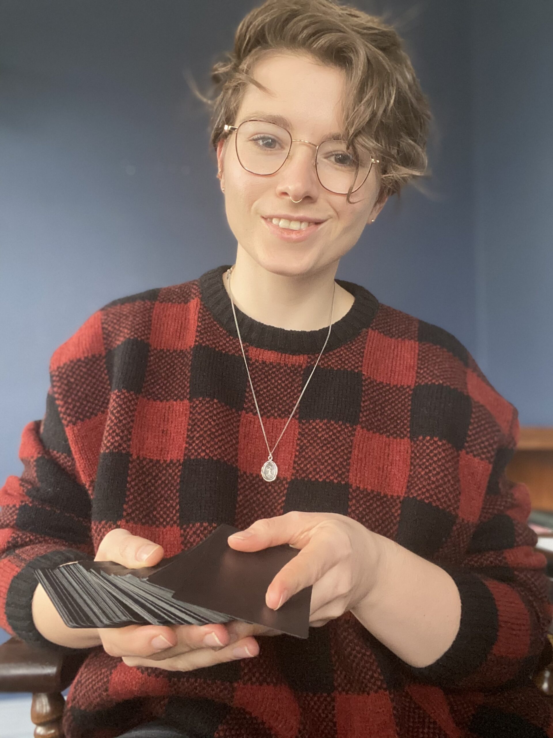 A picture of Lex wearing glasses and holding a deck of tarot cards. 