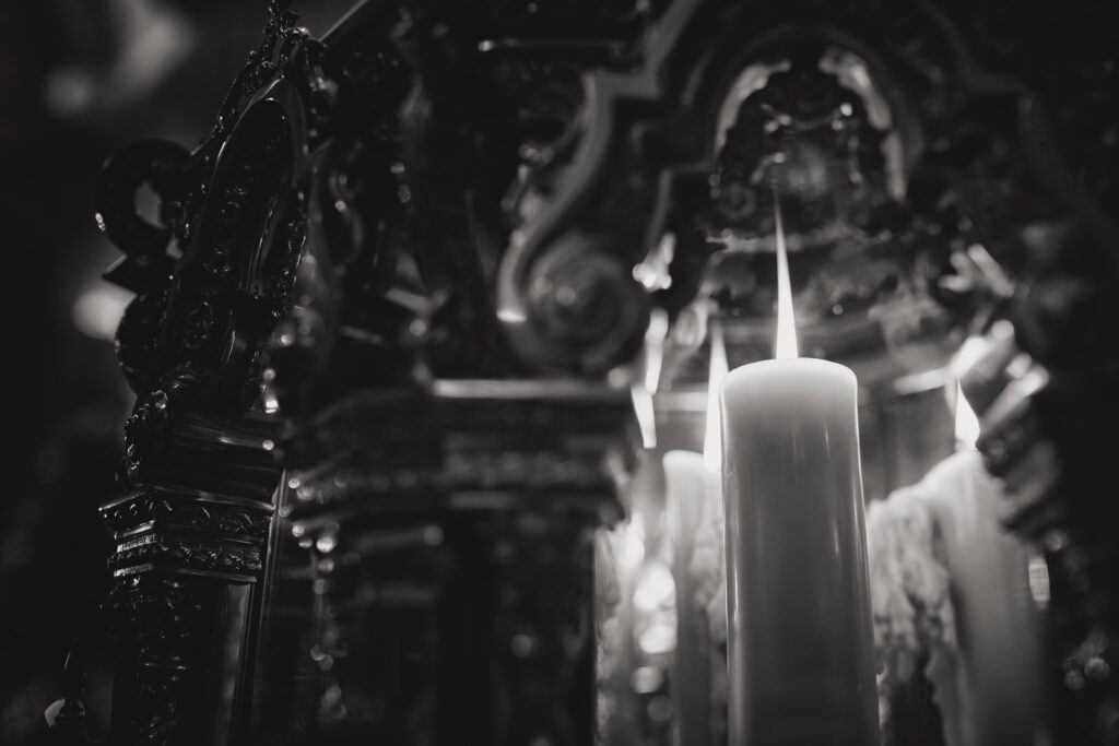 Black and white image of lit pillar candles before a gilt altar